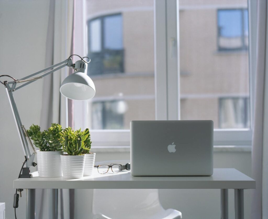 Contact us new Bright modern workspace with laptop, potted plants, and desk lamp near a window.